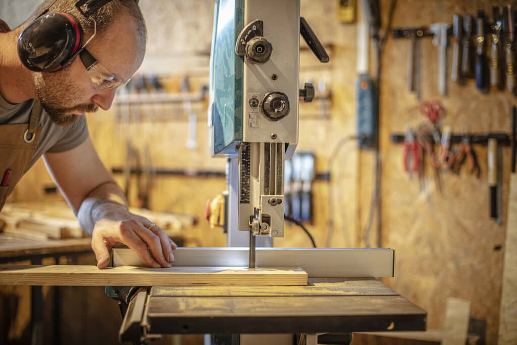 portrait of a carpenter inside his carpentry workshop using a band saw.